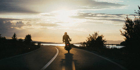 Riding a motorcycle on a road with the Alaska midnight sun.